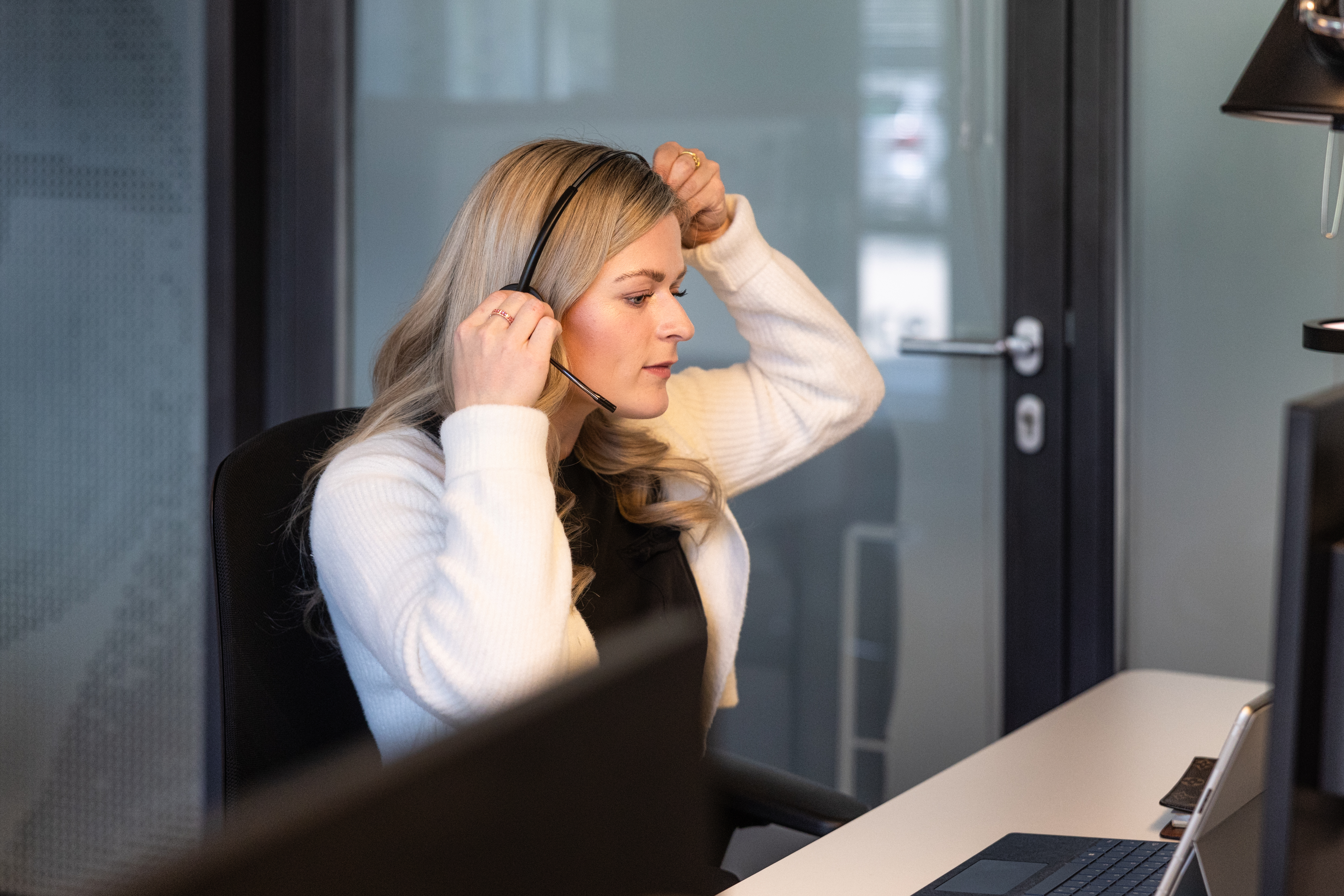 Frau sitzt am Schreibtisch und setzt gerade ihr Headset auf, um in Kontakt mit den Kunden zu treten.