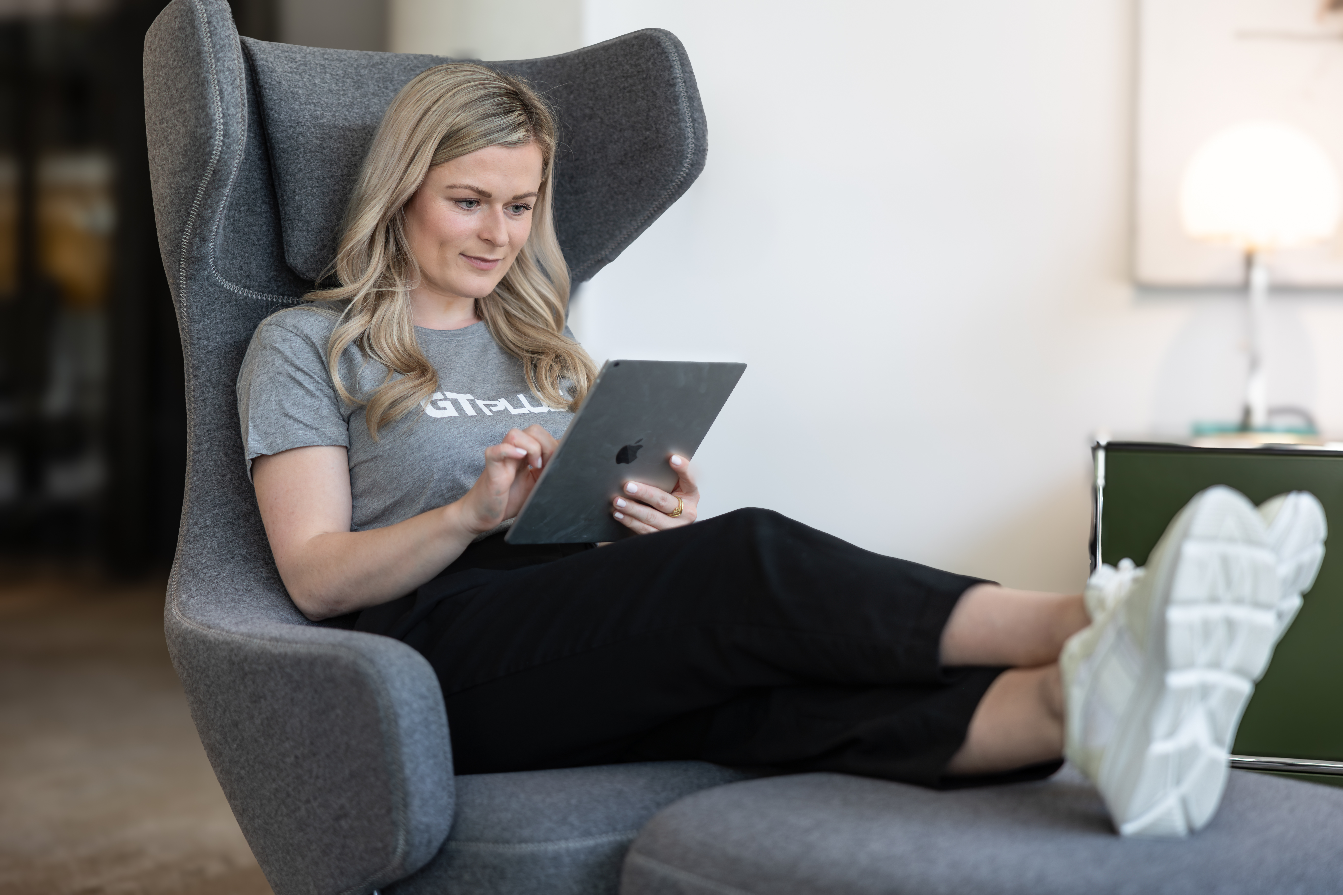 Frau sitzt entspannt in einem Sessel und ist konzentriert am Tablet.