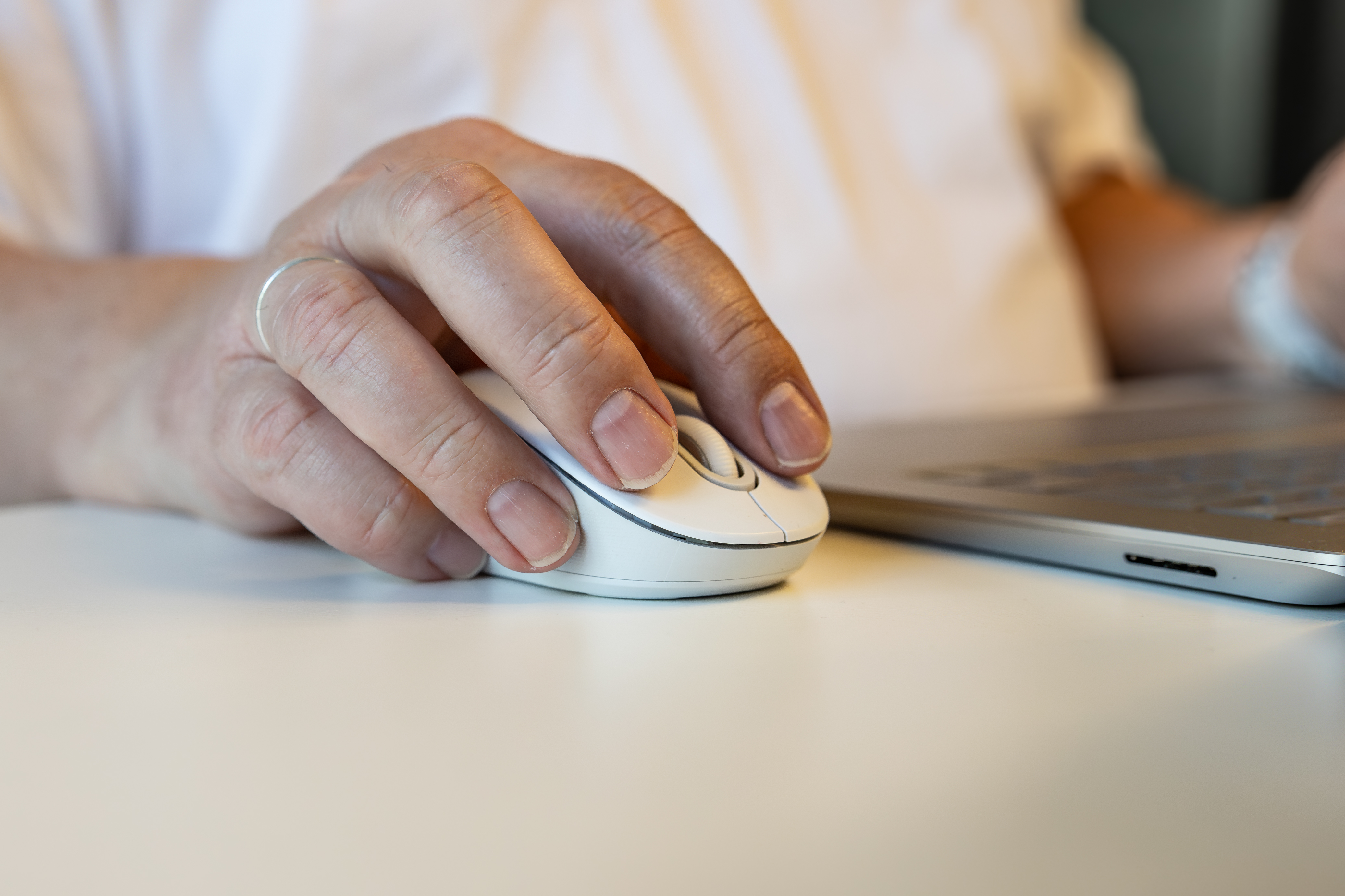 Mann hat seine Hand auf der Maus auf dem Schreibtisch, man sieht den Laptop im Hintergrund.